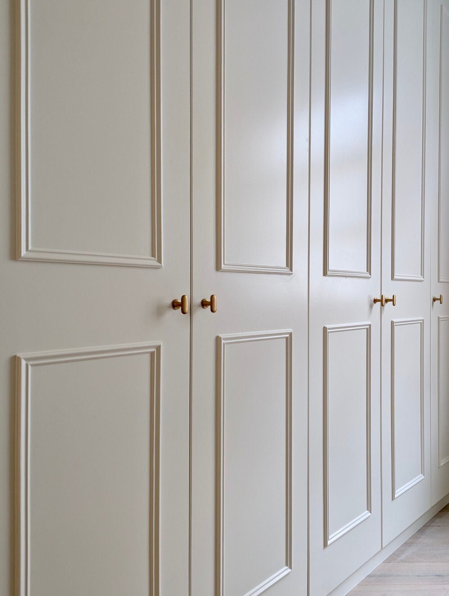 White paneled closet doors with brass knobs in a bright hallway