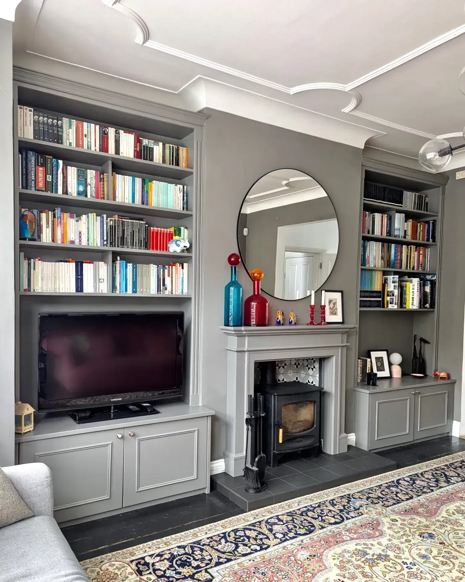 Gray living room with built-in bookshelves, fireplace, TV, mirror, and patterned rug