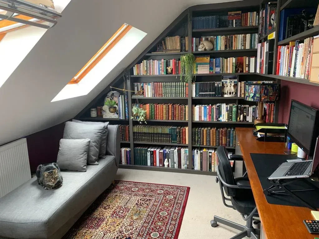 Small attic office with bookshelves, desk, gray sofa, and skylight window.