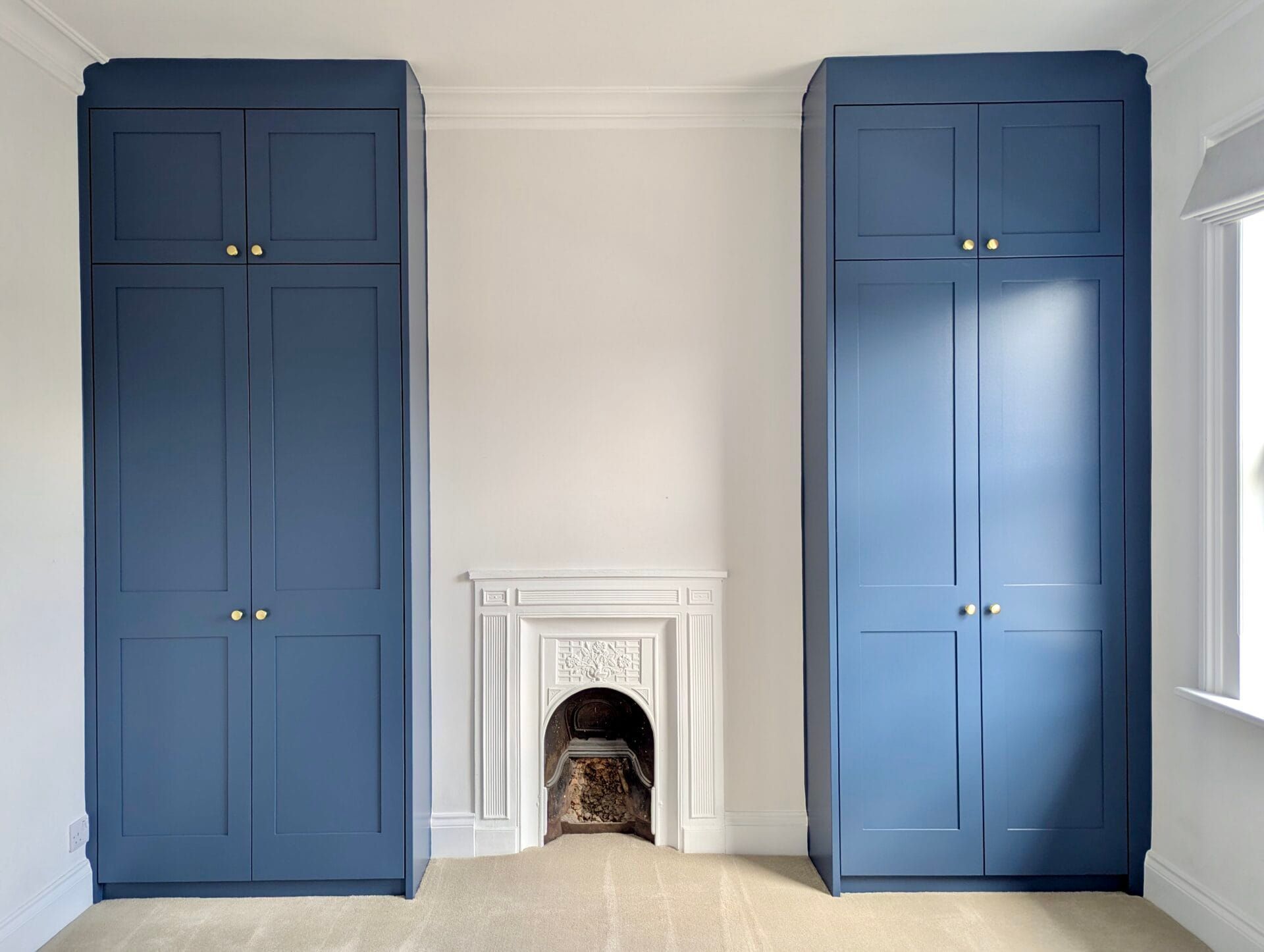 Blue built-in cabinets flank a small white fireplace in a bright room.