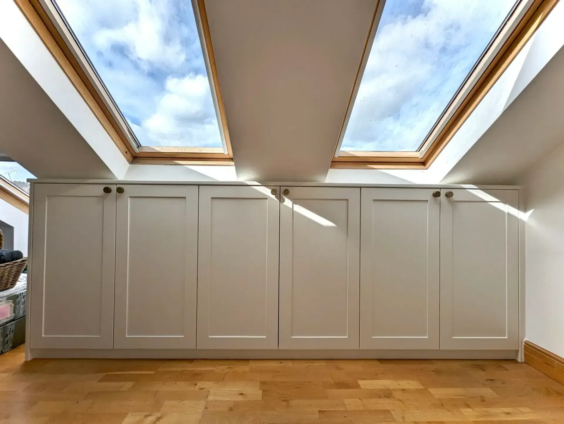 White built-in cabinets beneath skylight windows in a bright attic room with wood floor.