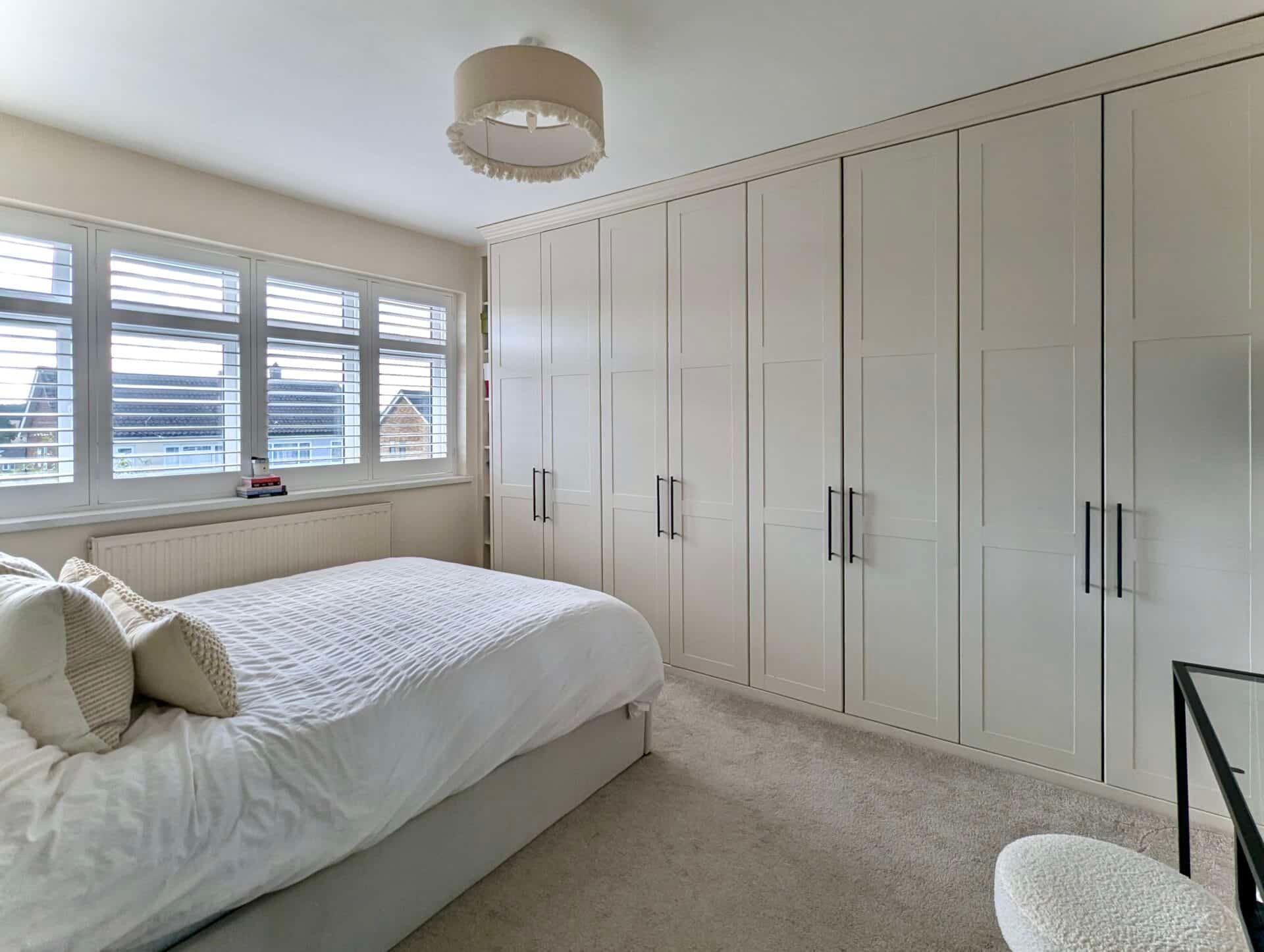 Bright bedroom with white built-in wardrobes, bed, window blinds, and beige carpet
