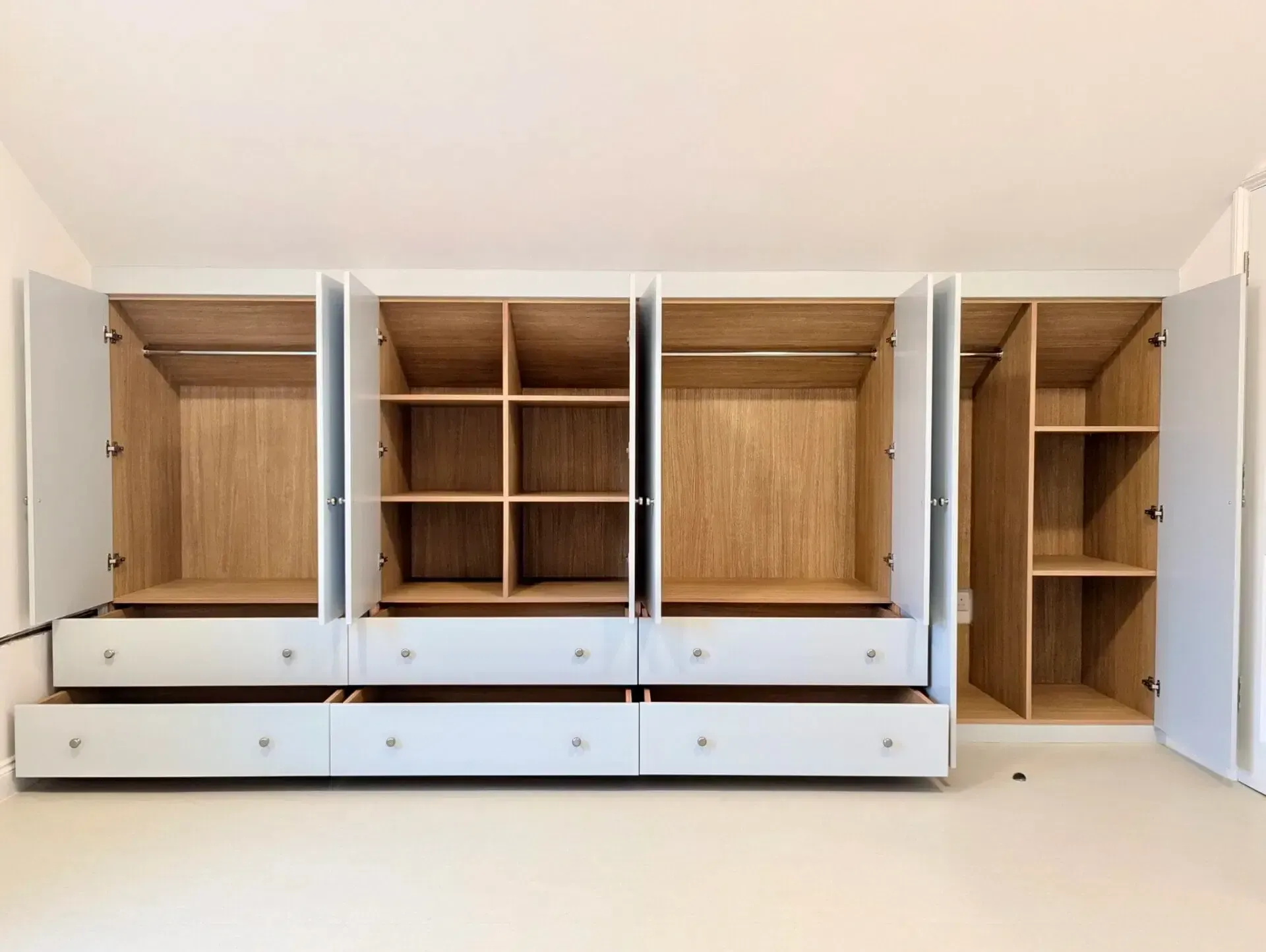 Open white wardrobe with empty wooden cabinets and drawers in a bright room
