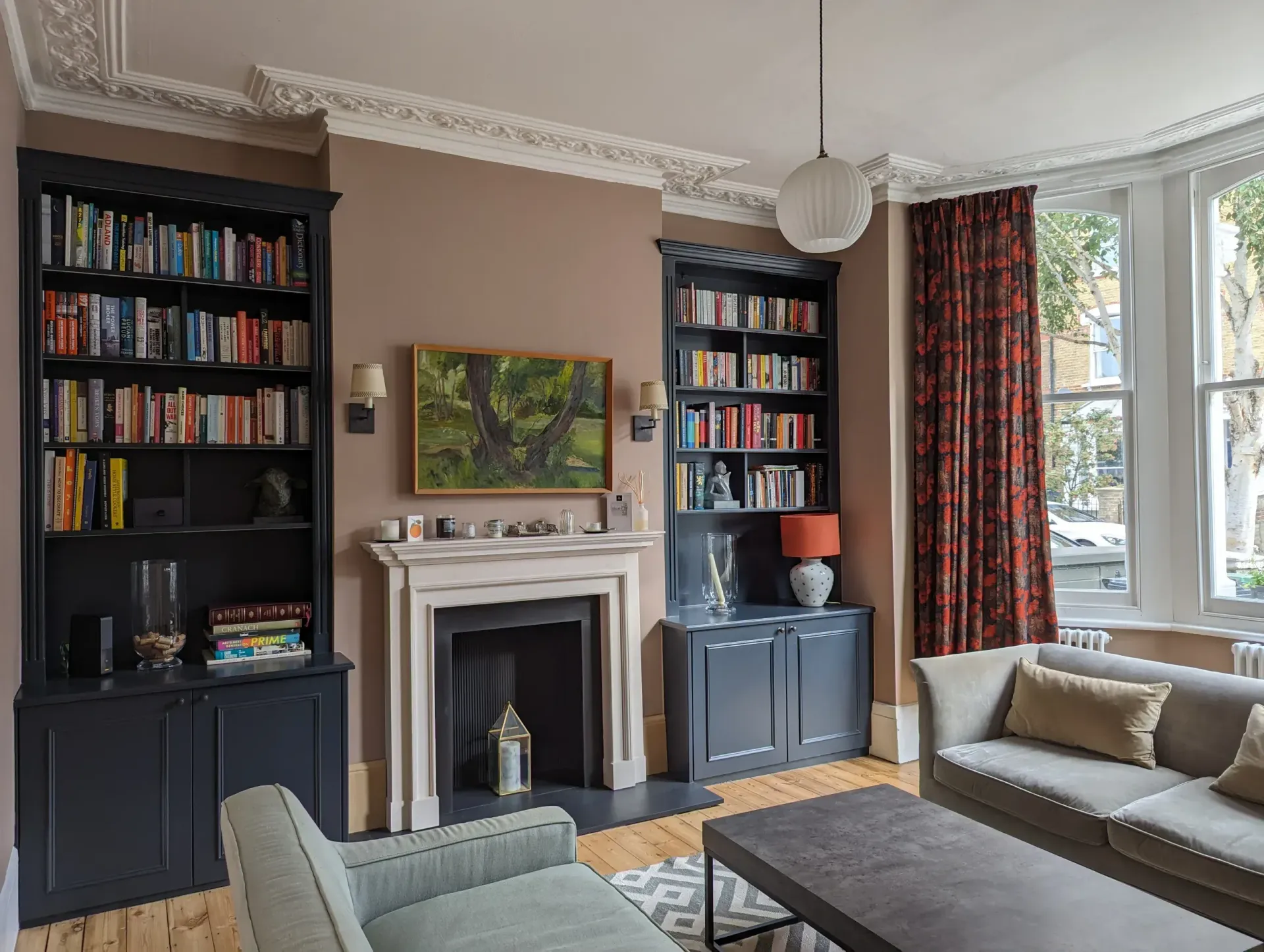 Cozy living room with two bookcases, fireplace, gray sofa, and bay window with red curtains