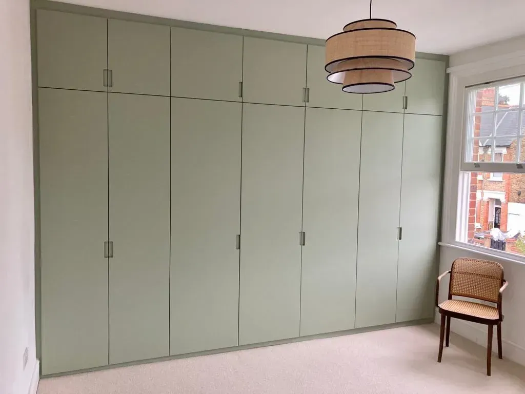 Built-in sage green storage cabinets in a bright room with a woven chair by the window.