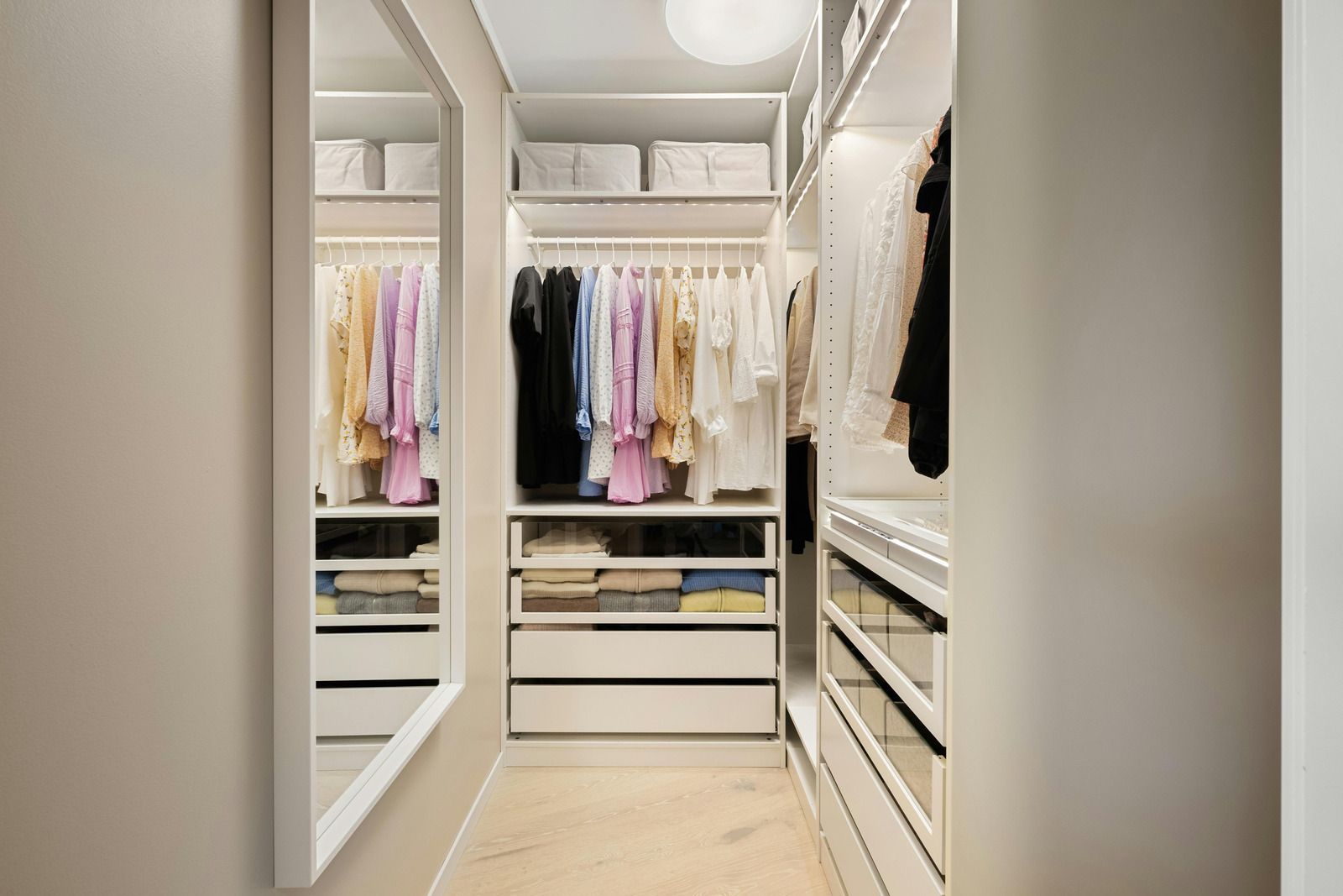Spacious walk-in closet with white shelving, hanging clothes, drawers, and full-length mirrors.