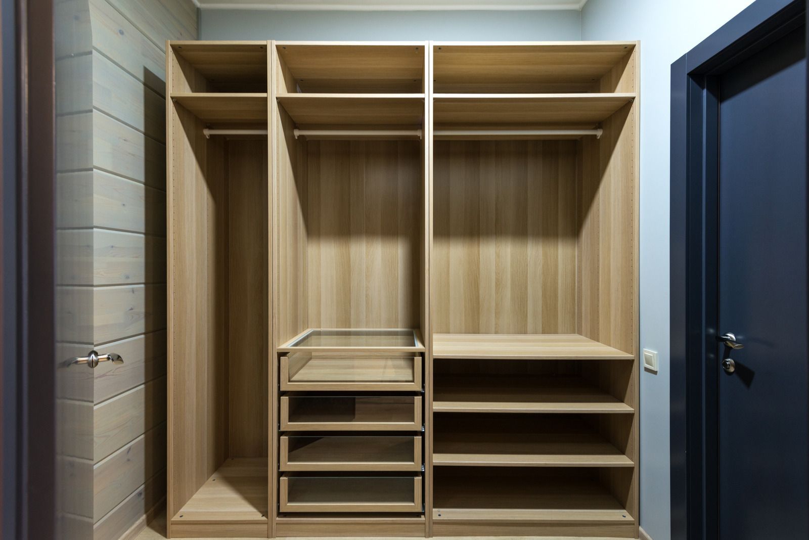 Wooden built-in wardrobe with open shelves, hanging rods, and drawers in a hallway.
