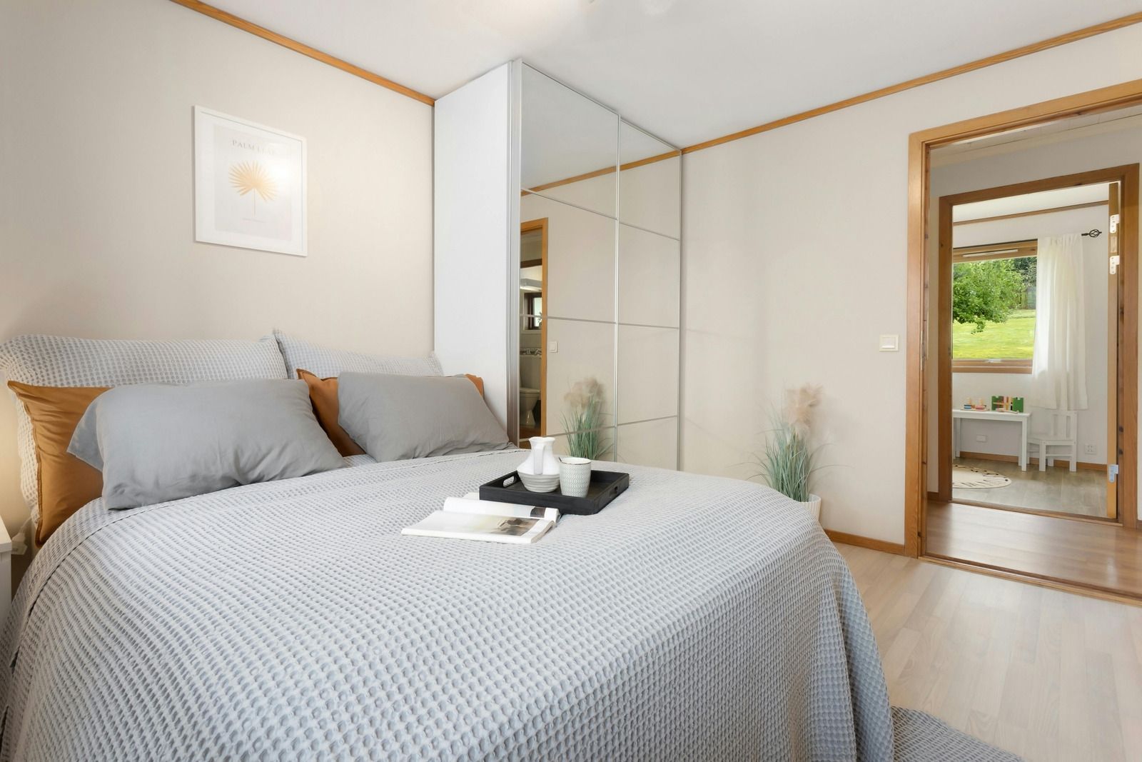 Bright bedroom with gray bedspread, mirrored closet, and doorway to a sunlit room