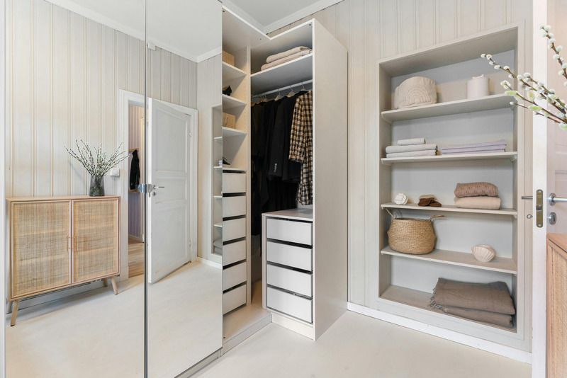 Bright walk-in closet with mirrored doors, white shelves, drawers, and hanging clothes