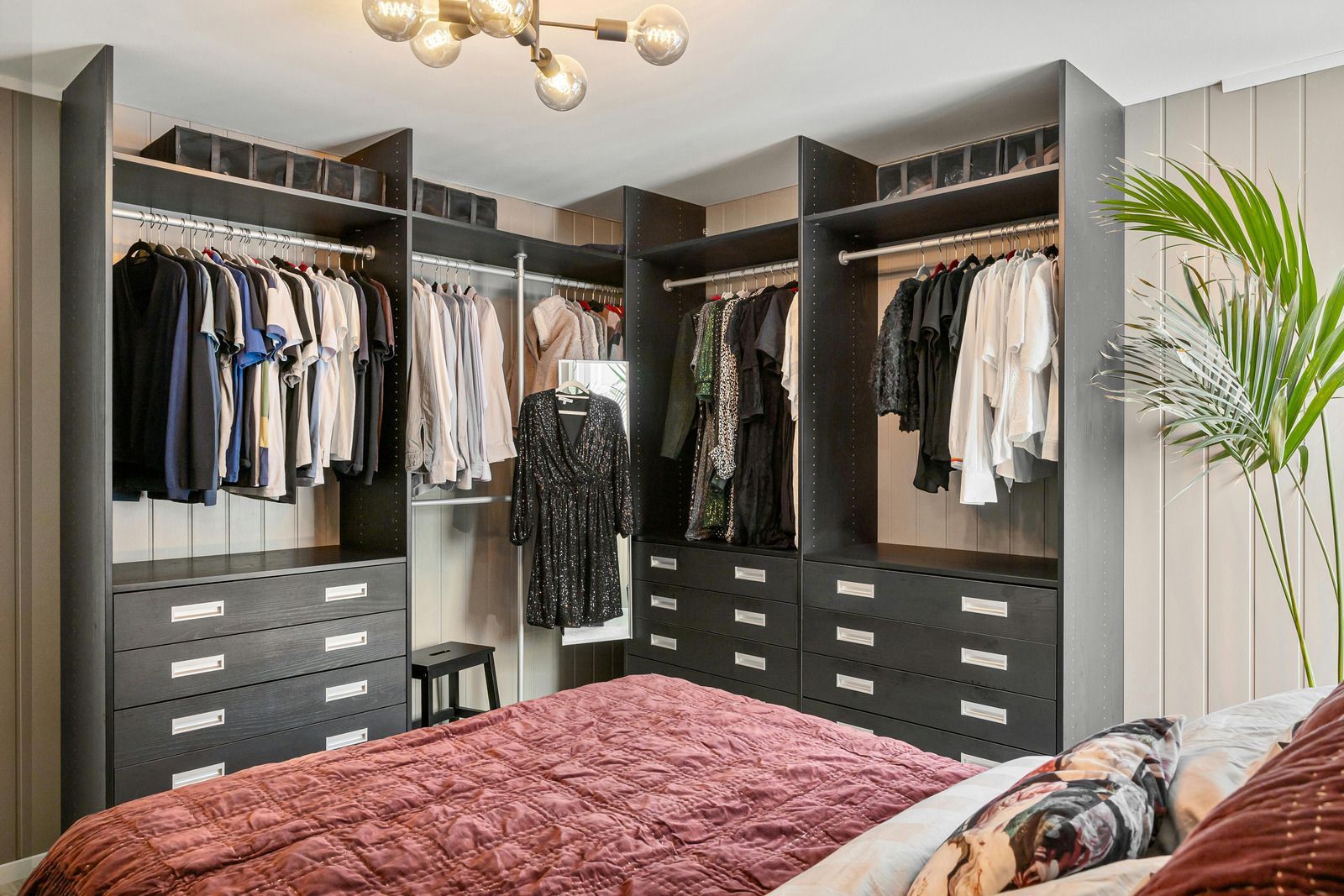Walk-in closet with hanging clothes, drawers, and a bed in the foreground