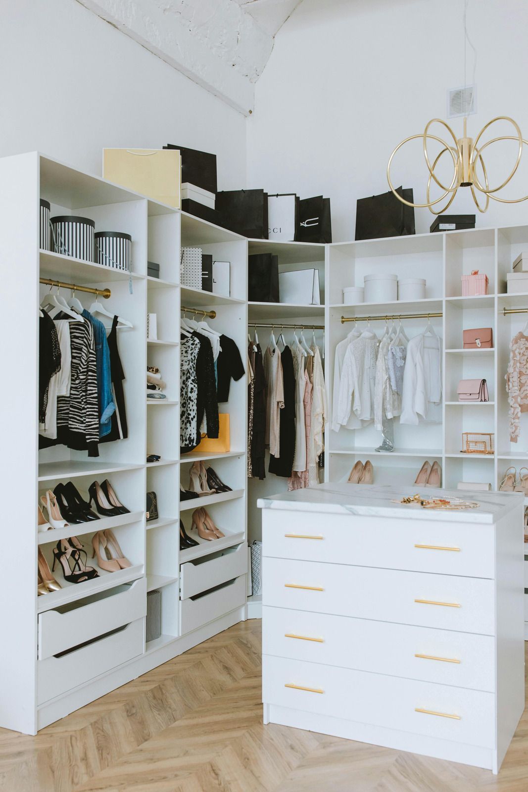Bright white walk-in closet with open shelves, hanging clothes, and a central drawer dresser