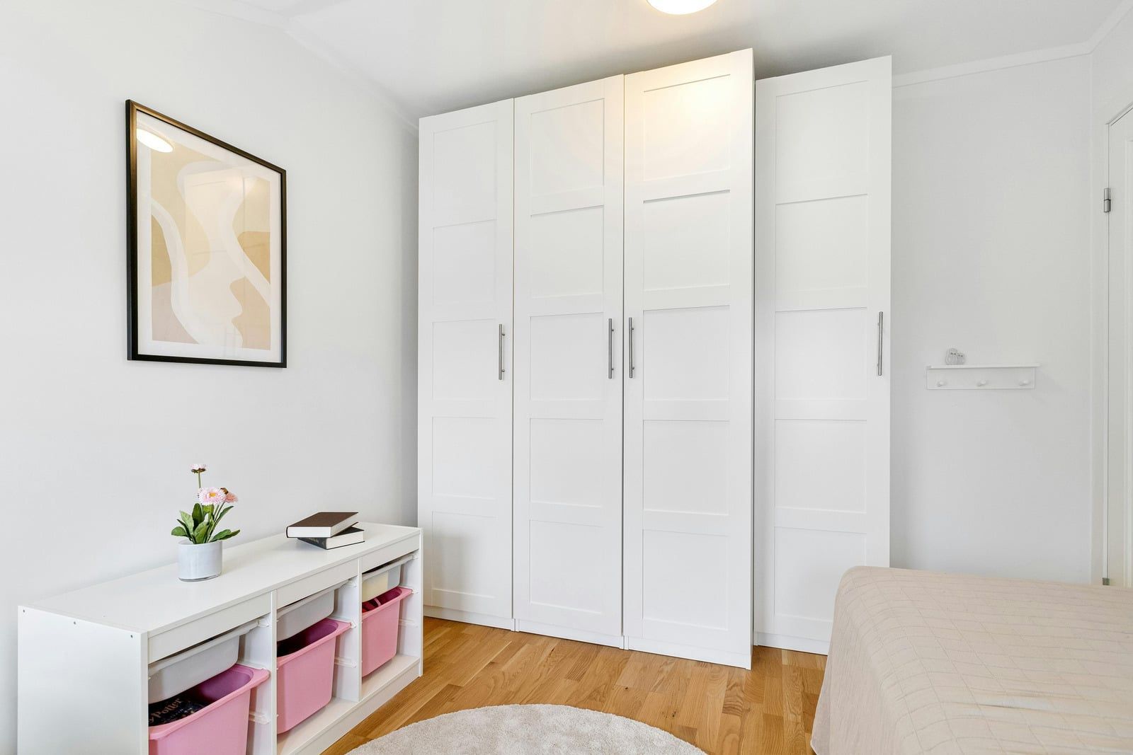 Bright white bedroom with built-in cabinets, a small shelf, and light wood flooring.