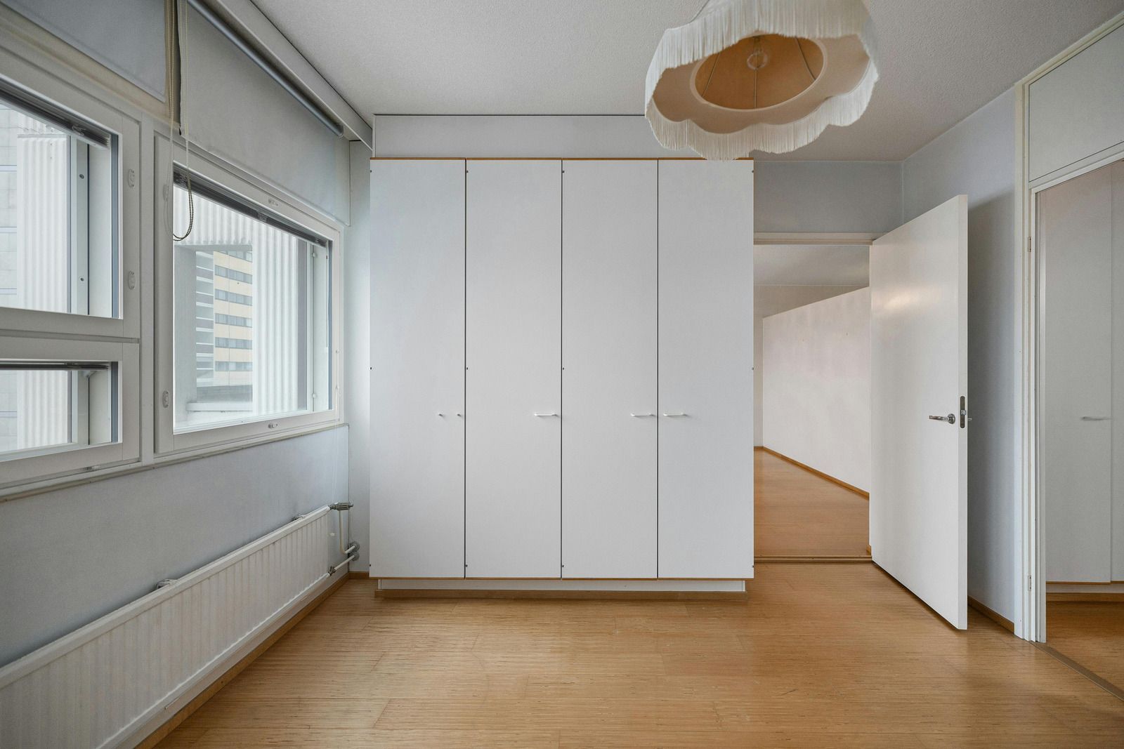 Empty bright room with white wardrobes, wood floor, windows, and an open door to a stairwell