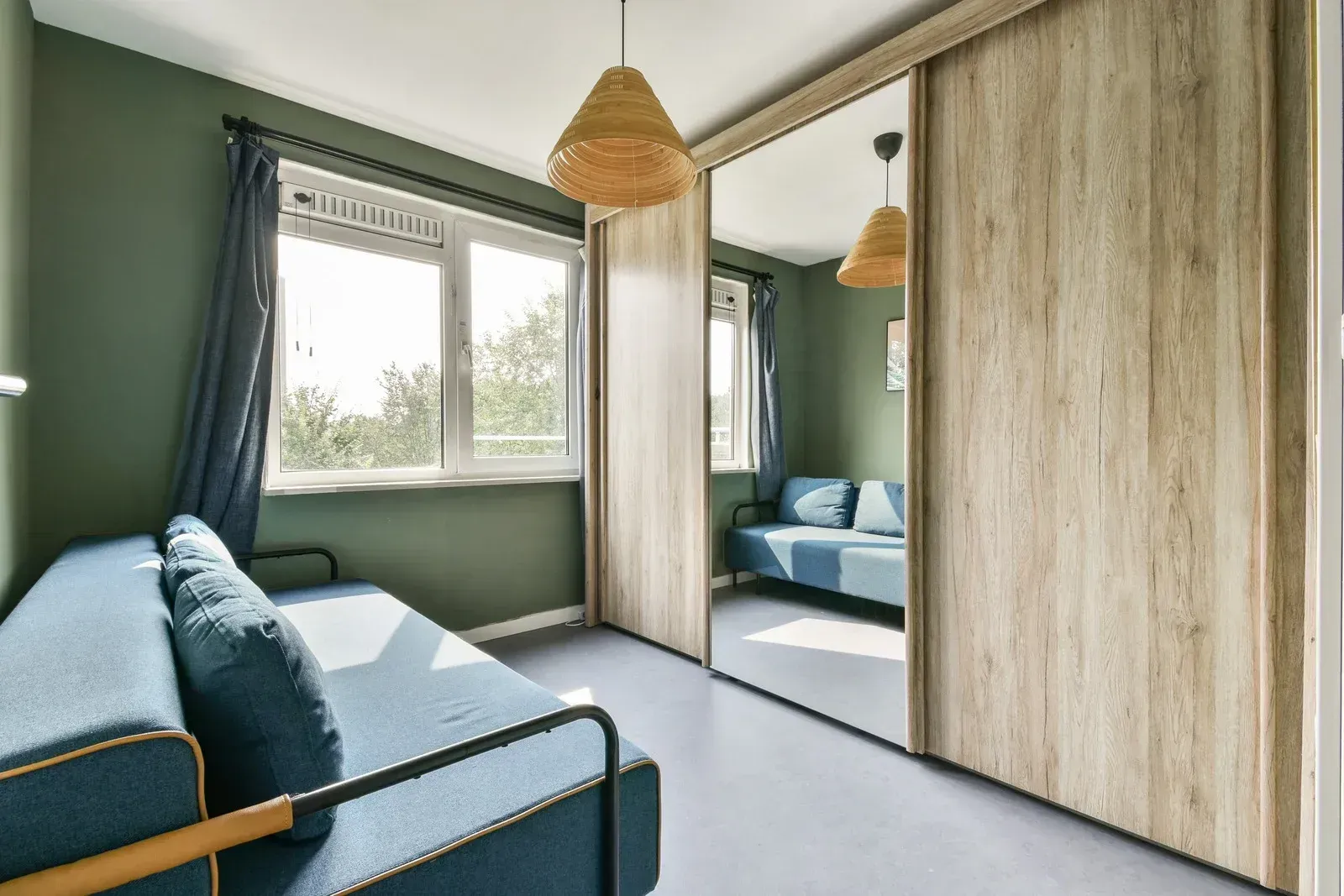 Bright bedroom with blue sofa, mirrored wardrobe, and large window by green walls