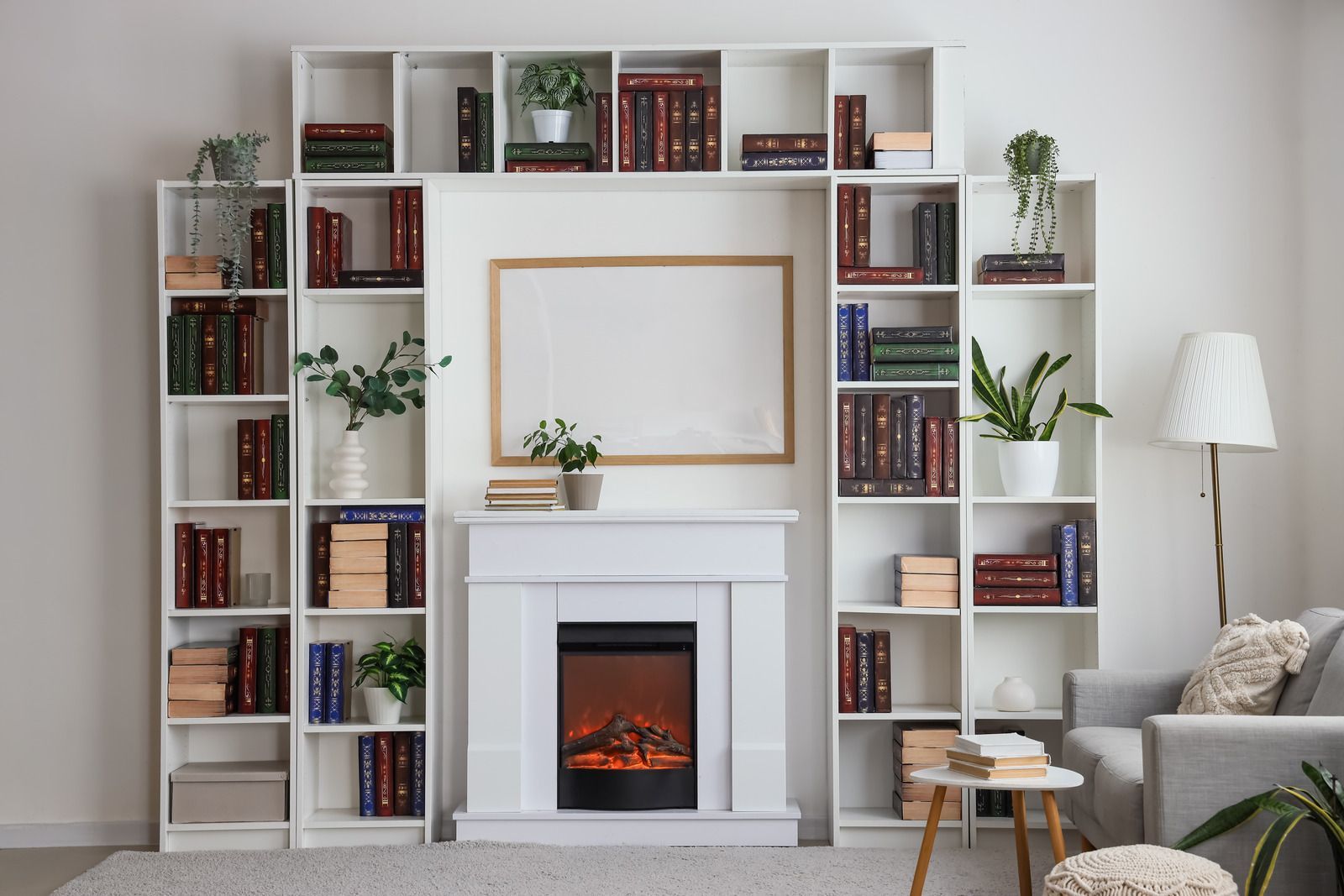 Living room with white built-in bookshelves, a fireplace, framed art, and a lamp beside a sofa.