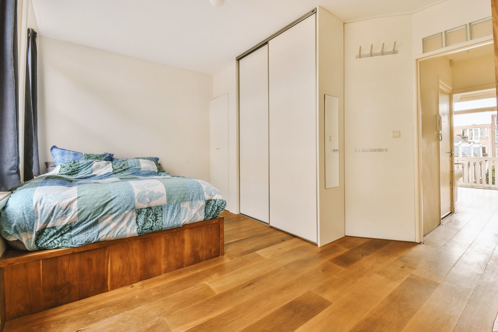 Bright bedroom with a wooden bed, white wardrobe, and sunlit hardwood floor