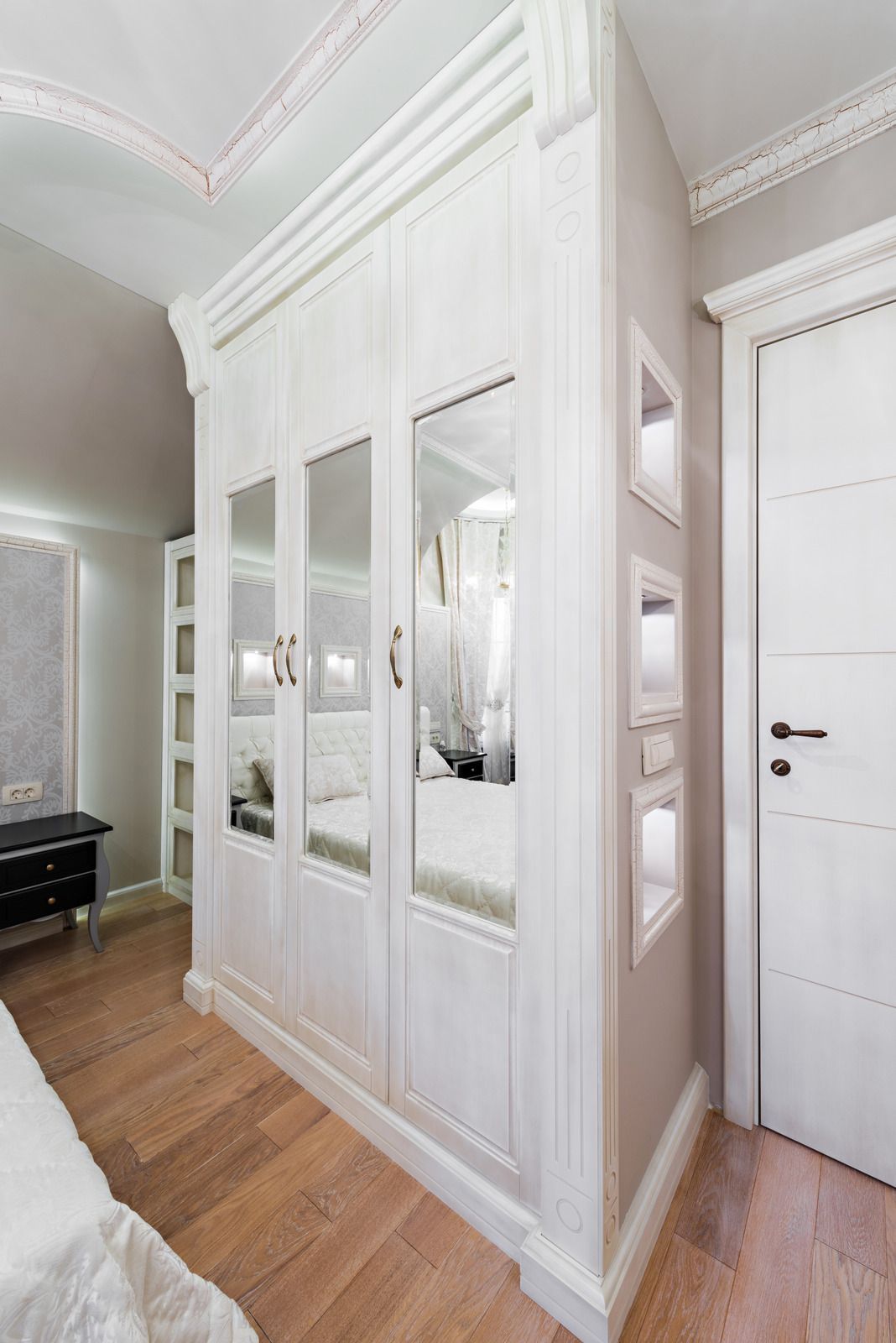 White built-in mirrored wardrobe in a bright hallway with wood flooring and a white door