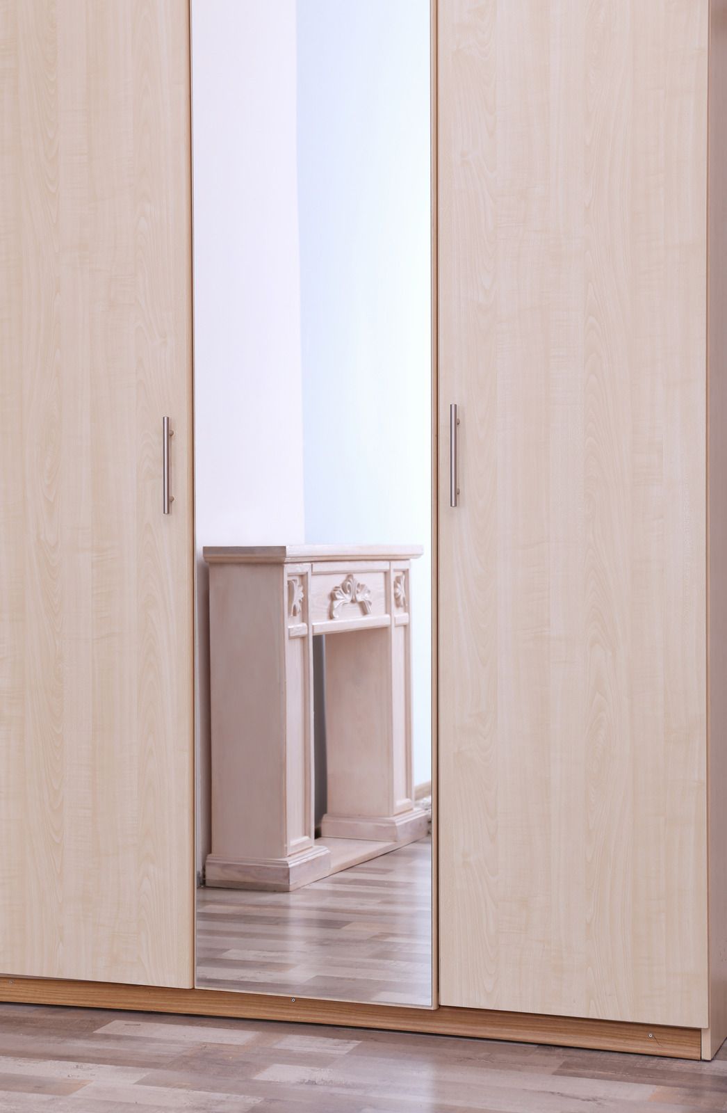 Light wood wardrobe with mirrored doors, reflecting a small desk in a bright room.