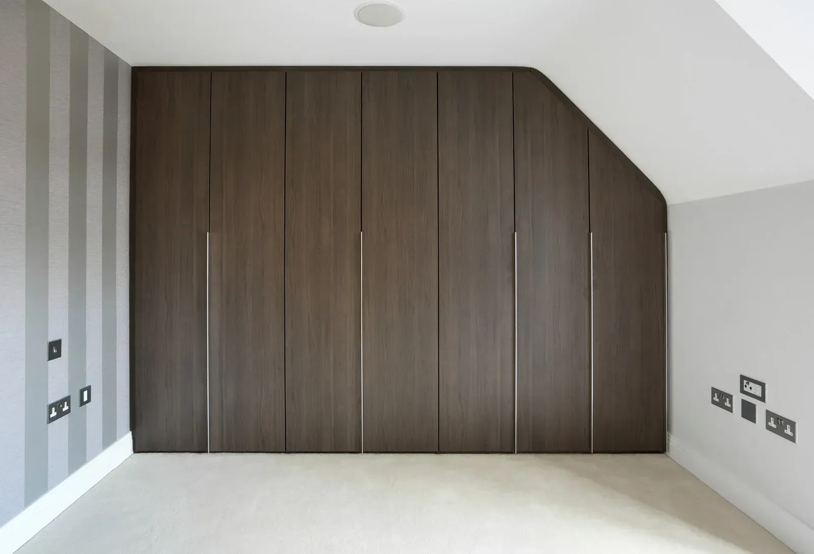 Minimalist bedroom with large dark wood built-in wardrobe and light gray walls