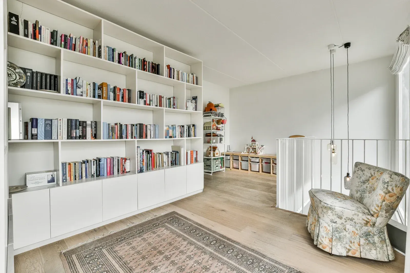 Bright home office with white built-in bookshelves, a rug, and a patterned armchair by a railing.