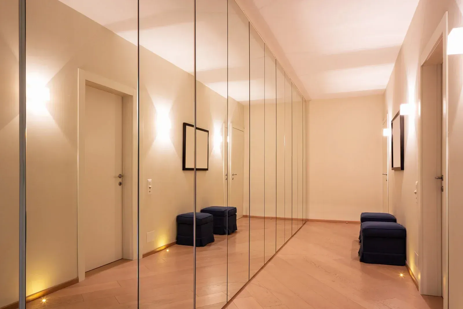 Minimalist mirrored hallway with beige walls, wood floor, and navy cushions along the sides