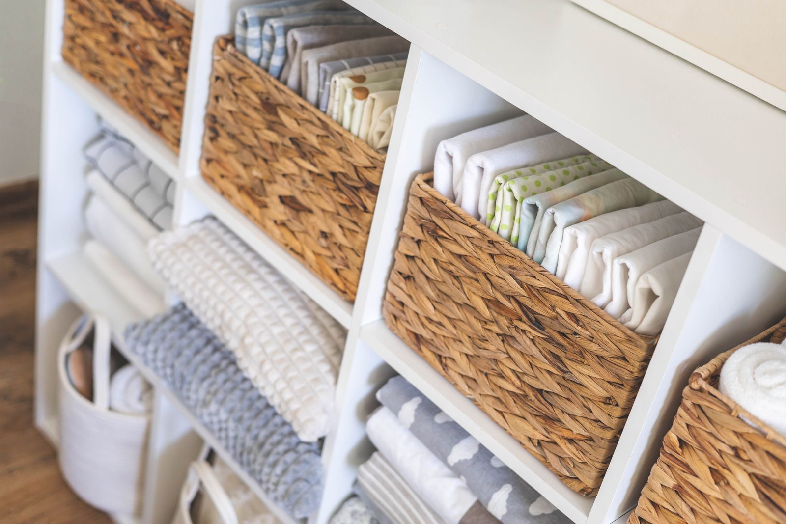 White cubby shelf with woven baskets and neatly folded towels in a bright room