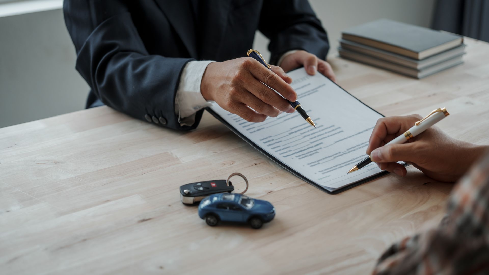 Persona firmando un contrato en una mesa con una llave de coche y un coche de juguete.