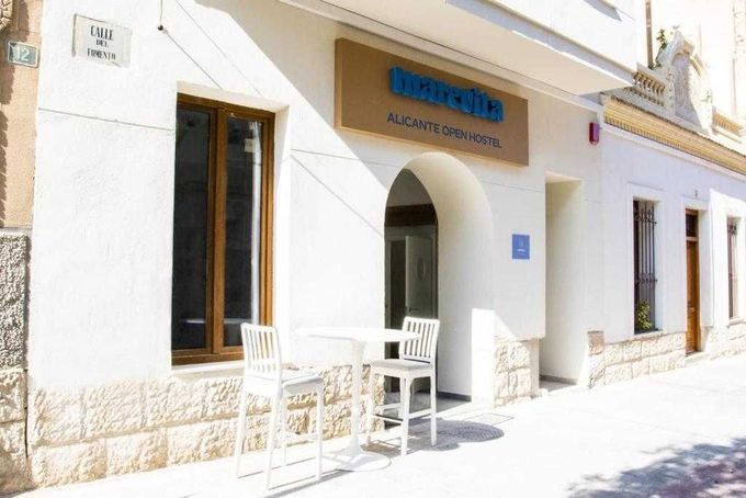 Exterior del Hotel Rullo con fachada blanca, cartel marrón y asientos al aire libre.