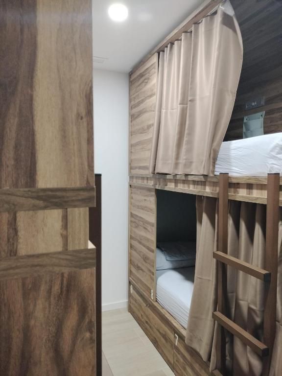 Literas en una habitación con paneles de madera y cortinas beige. Escalera visible.