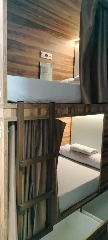 Literas en una habitación de albergue con paneles de madera, sábanas blancas y cortinas para mayor privacidad.