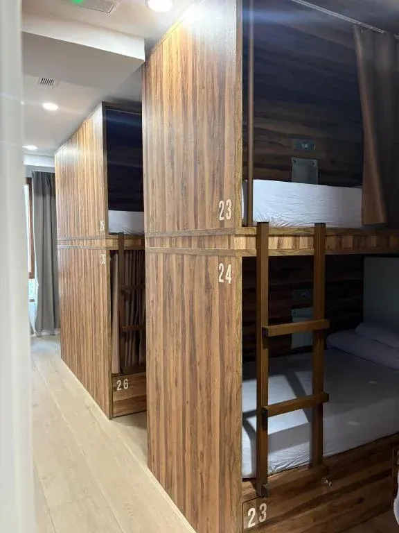 Literas en una habitación de hostal. Camas de madera con puertas numeradas. Escaleras que llevan a las literas superiores.