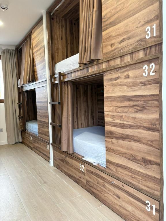 Literas de madera en una habitación de hostal, cada una con cortina. Se ven los números 31, 32 y 12.