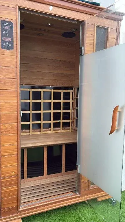 Sauna de madera con puerta de cristal parcialmente abierta. 