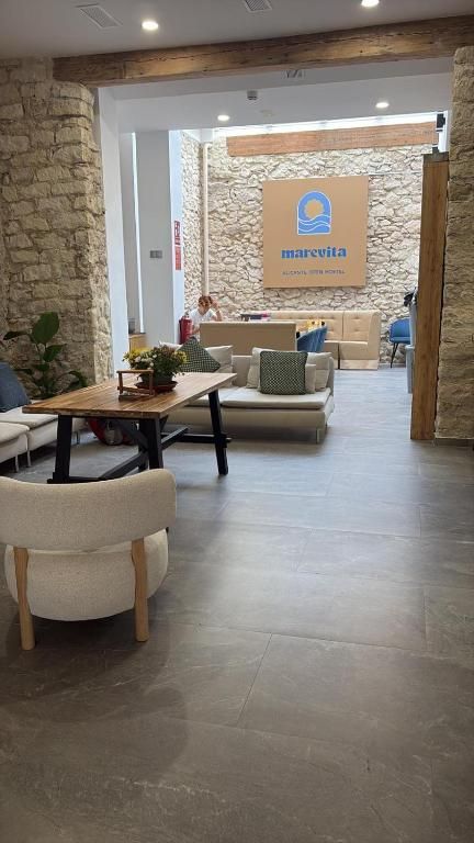 Vestíbulo con paredes de piedra, vigas de madera, asientos y una mesa. Un cartel en la pared del fondo dice 