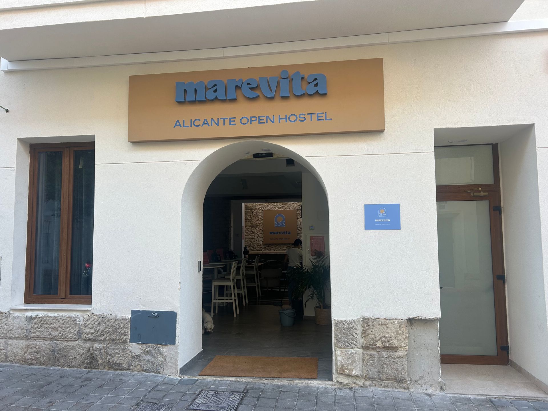 La entrada al Marevita Alicante Open Hostel, con un cartel marrón y una puerta arqueada.