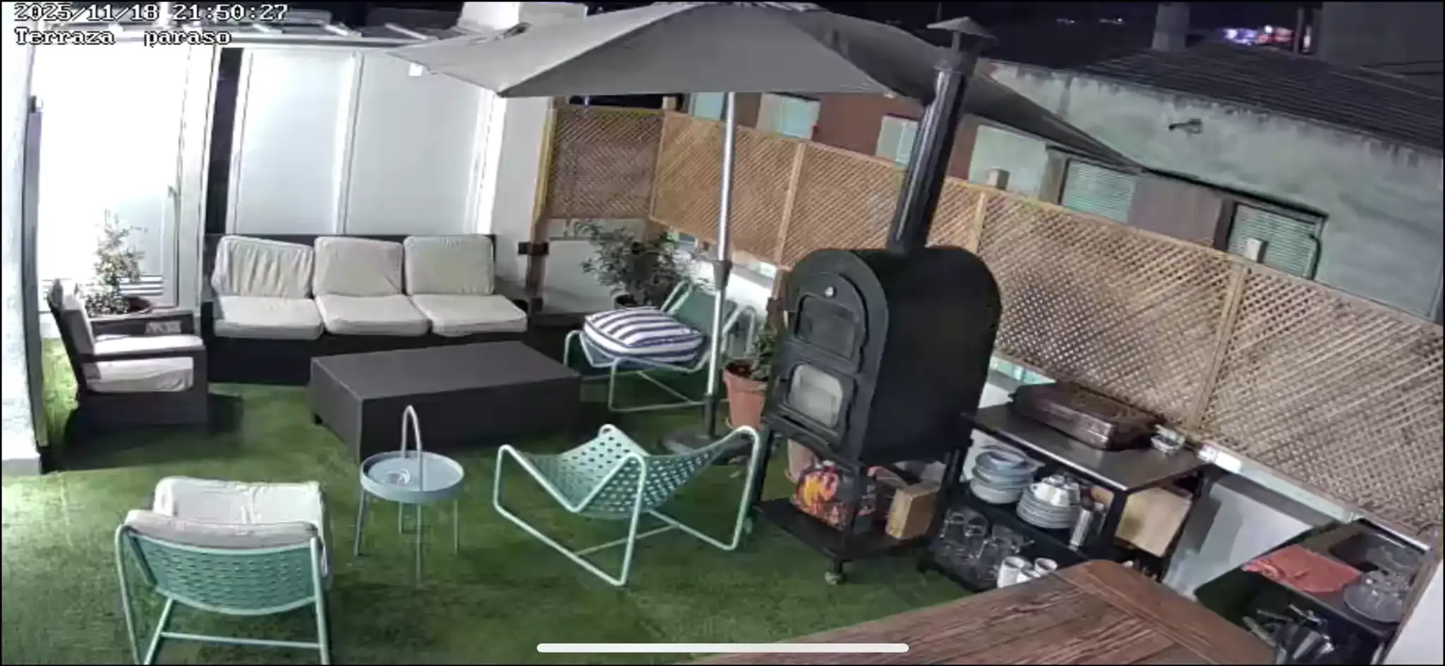 Un patio amueblado en la azotea por la noche con asientos, una chimenea y una gran sombrilla.