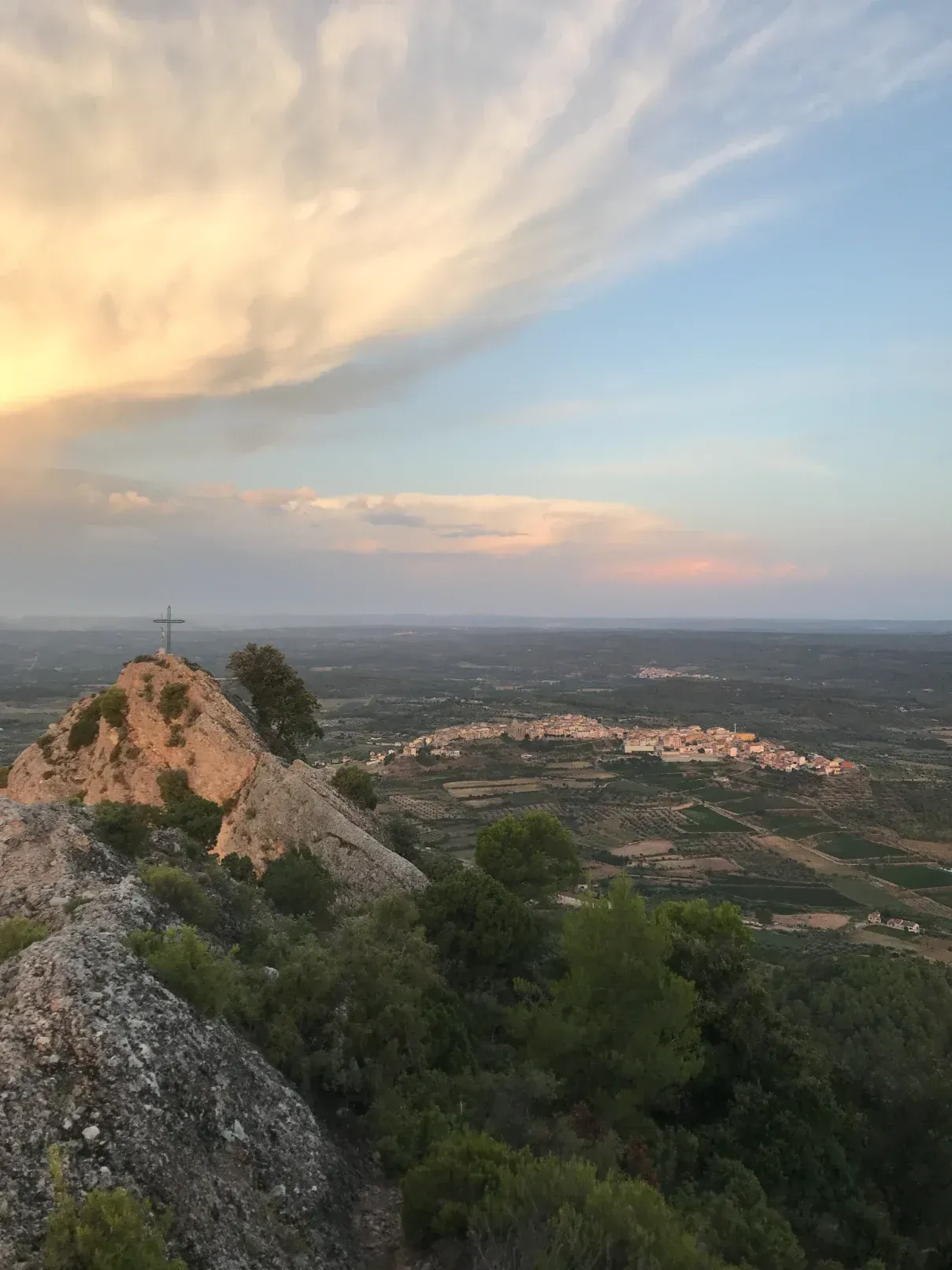 Vista de la posta de sol des d'un cim rocós amb vistes a una ciutat distant sota un cel ple de colors.