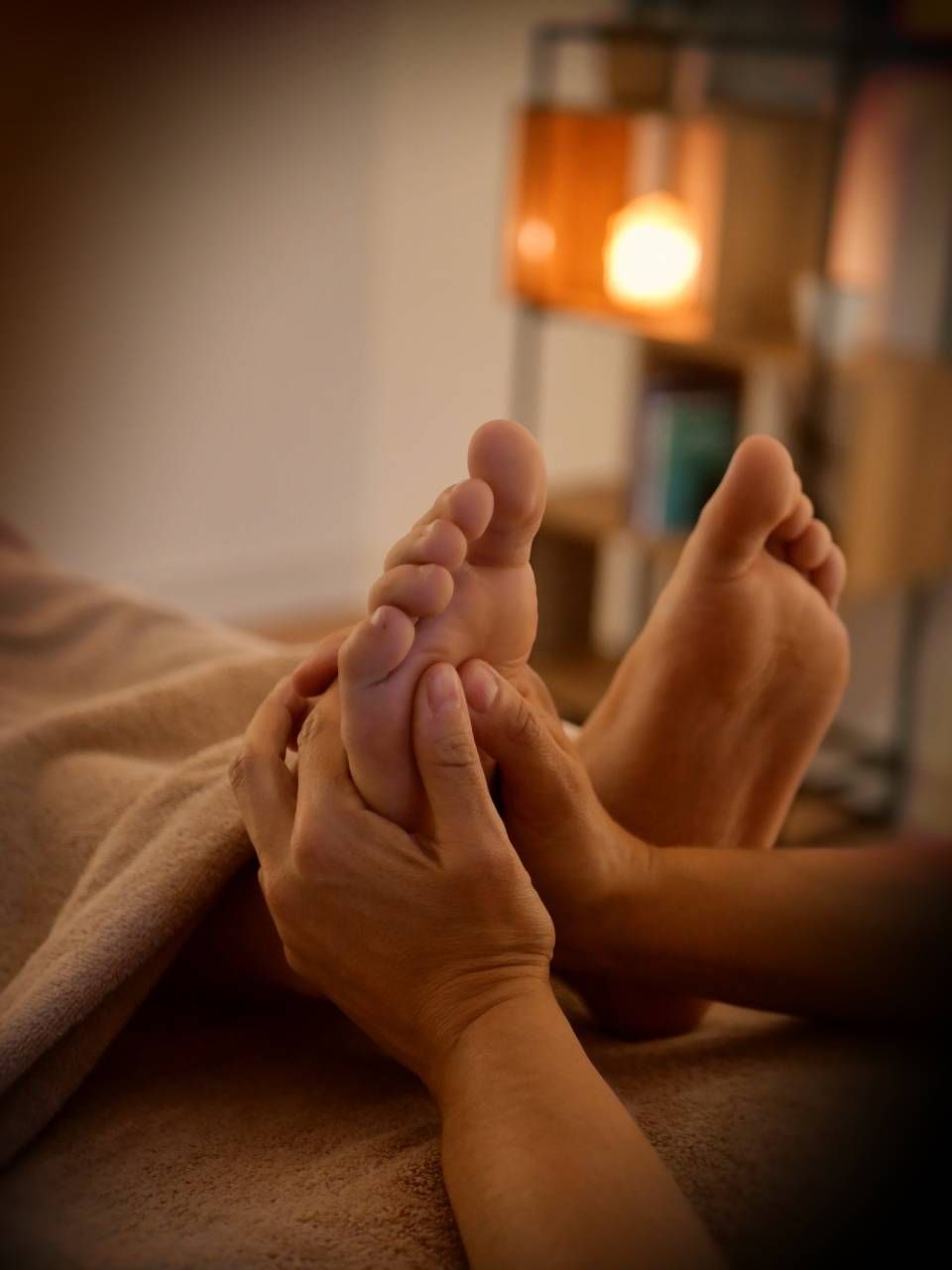 Des mains massent des pieds nus, à l'intérieur, sous une lumière tamisée.