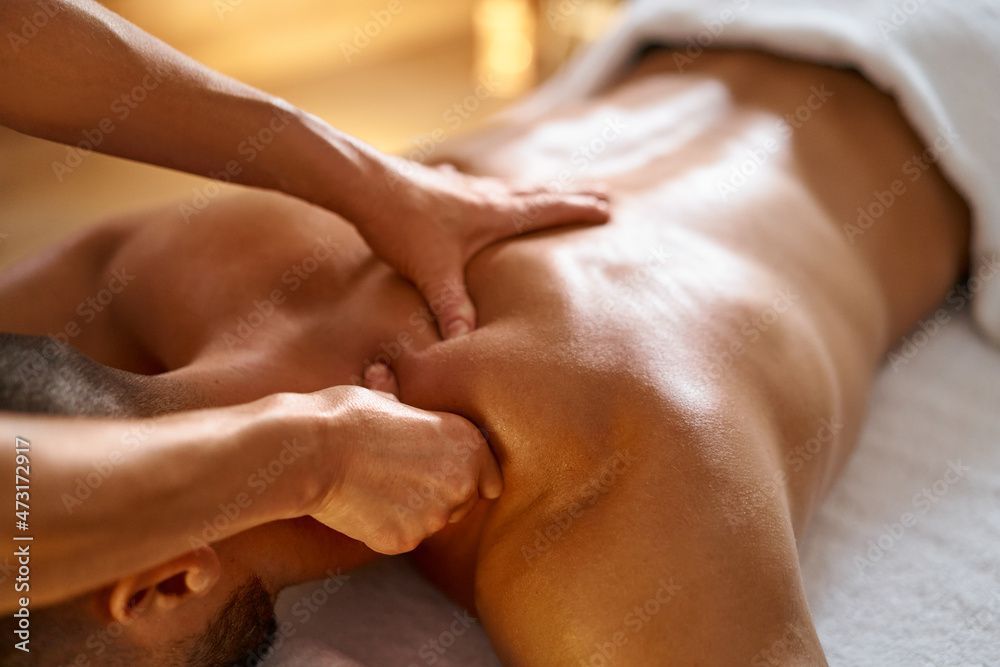 Une personne reçoit un massage des épaules sur une serviette blanche. Les mains du masseur exercent une pression.