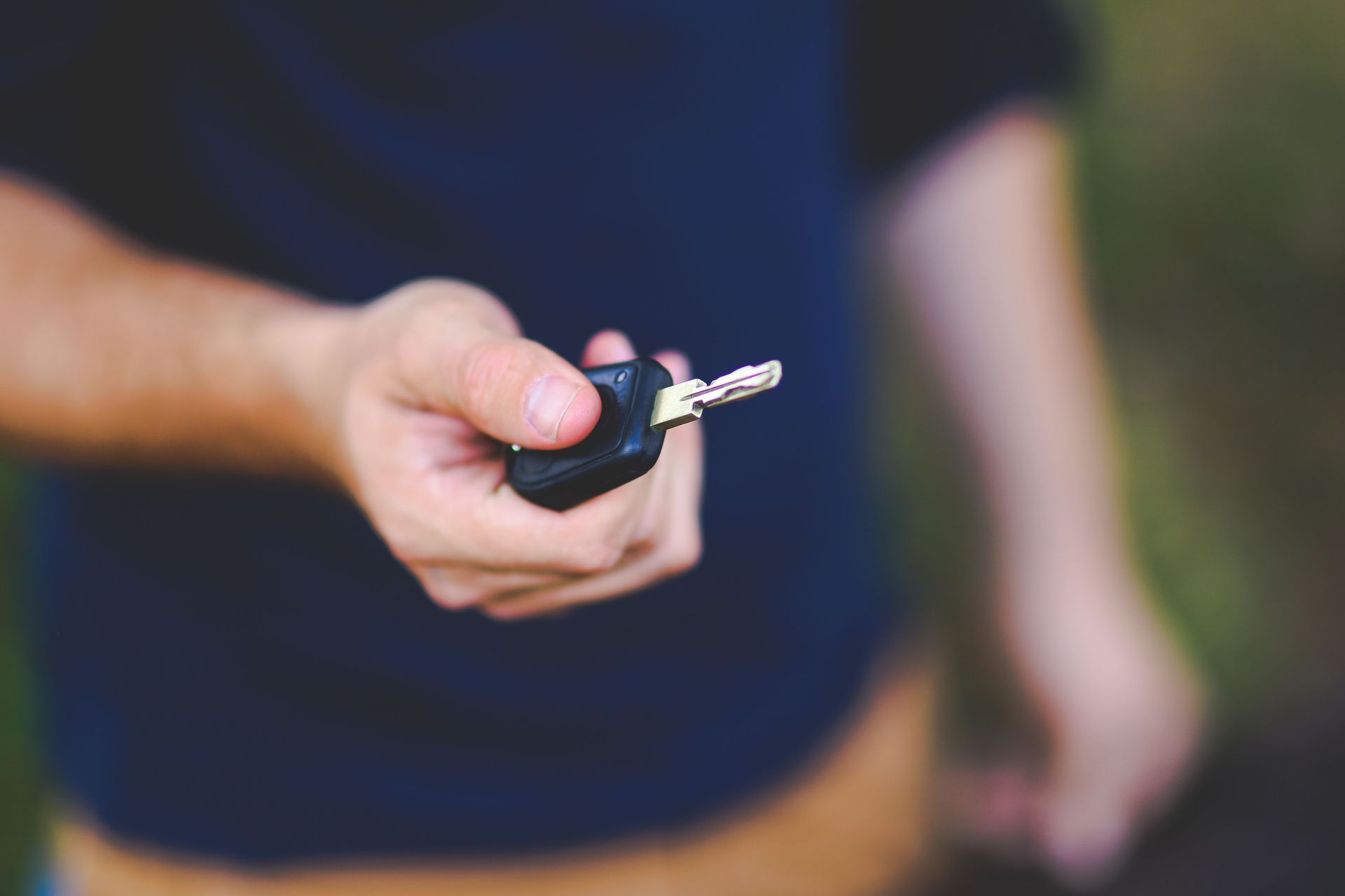 Main tenant une clé de voiture avec la clé métallique sortie, sur un fond sombre flou
