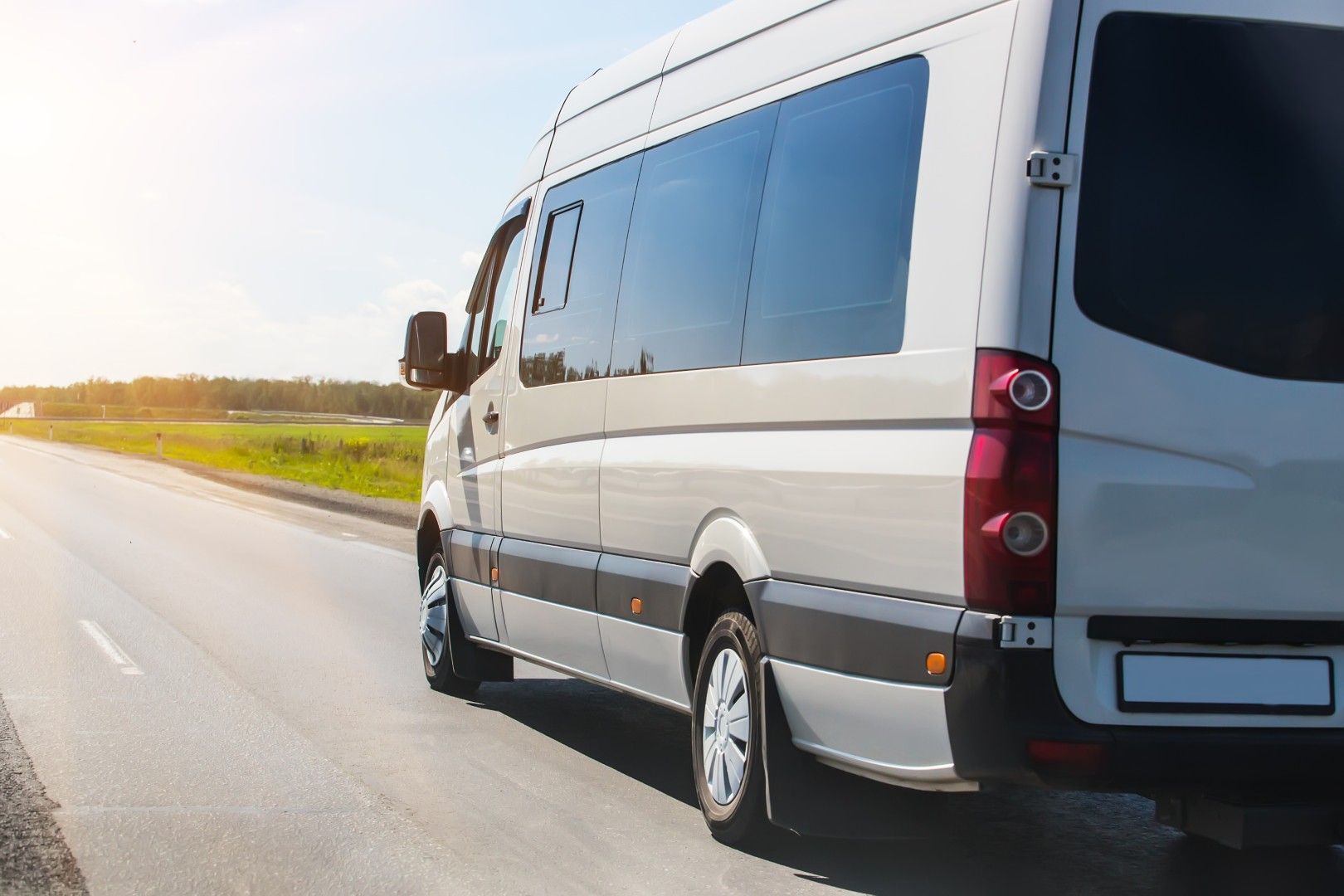 Un van blanc transportant des passagers roule sur une autoroute ensoleillée près de champs verdoyants