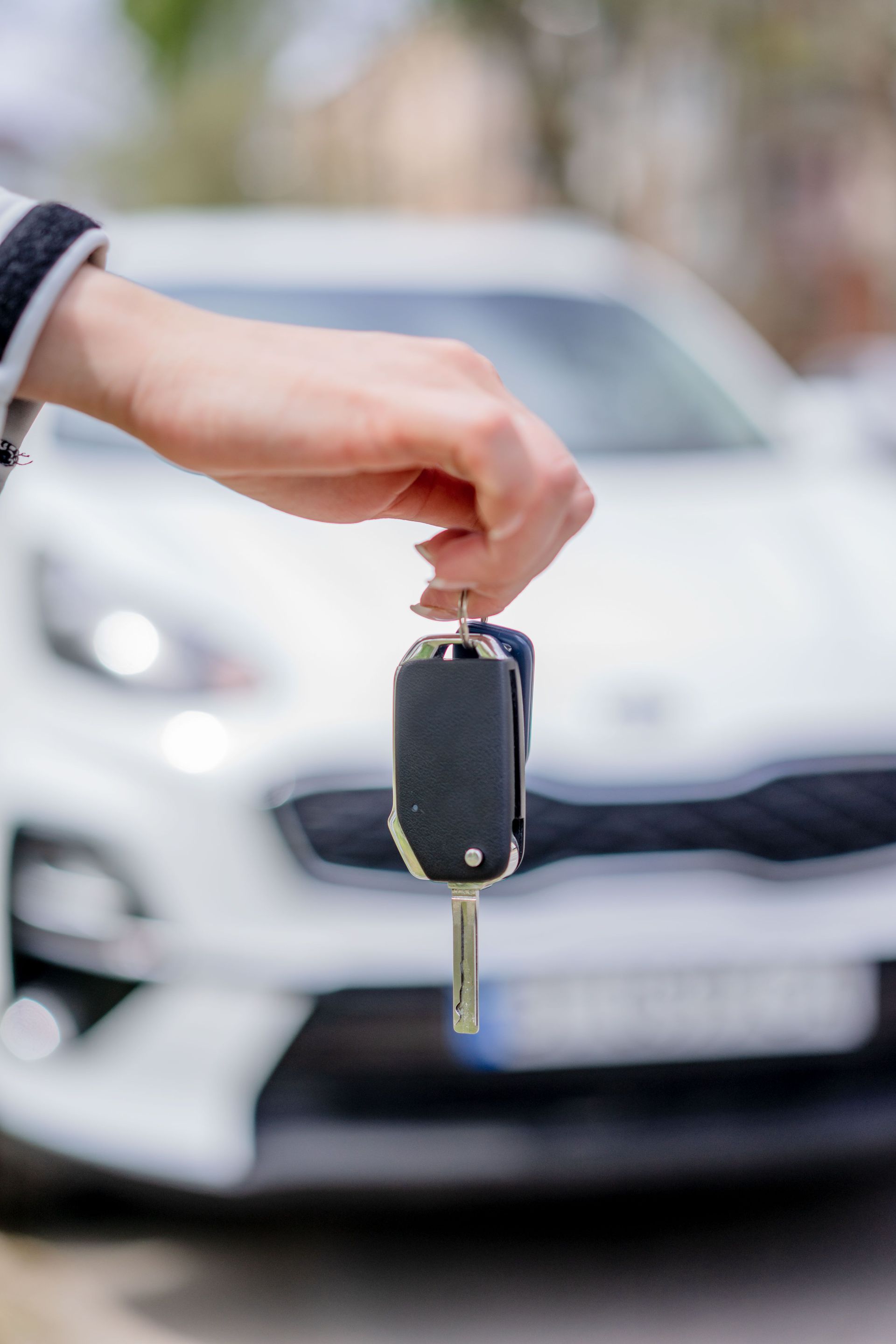 Main tenant une clé de voiture devant une voiture blanche