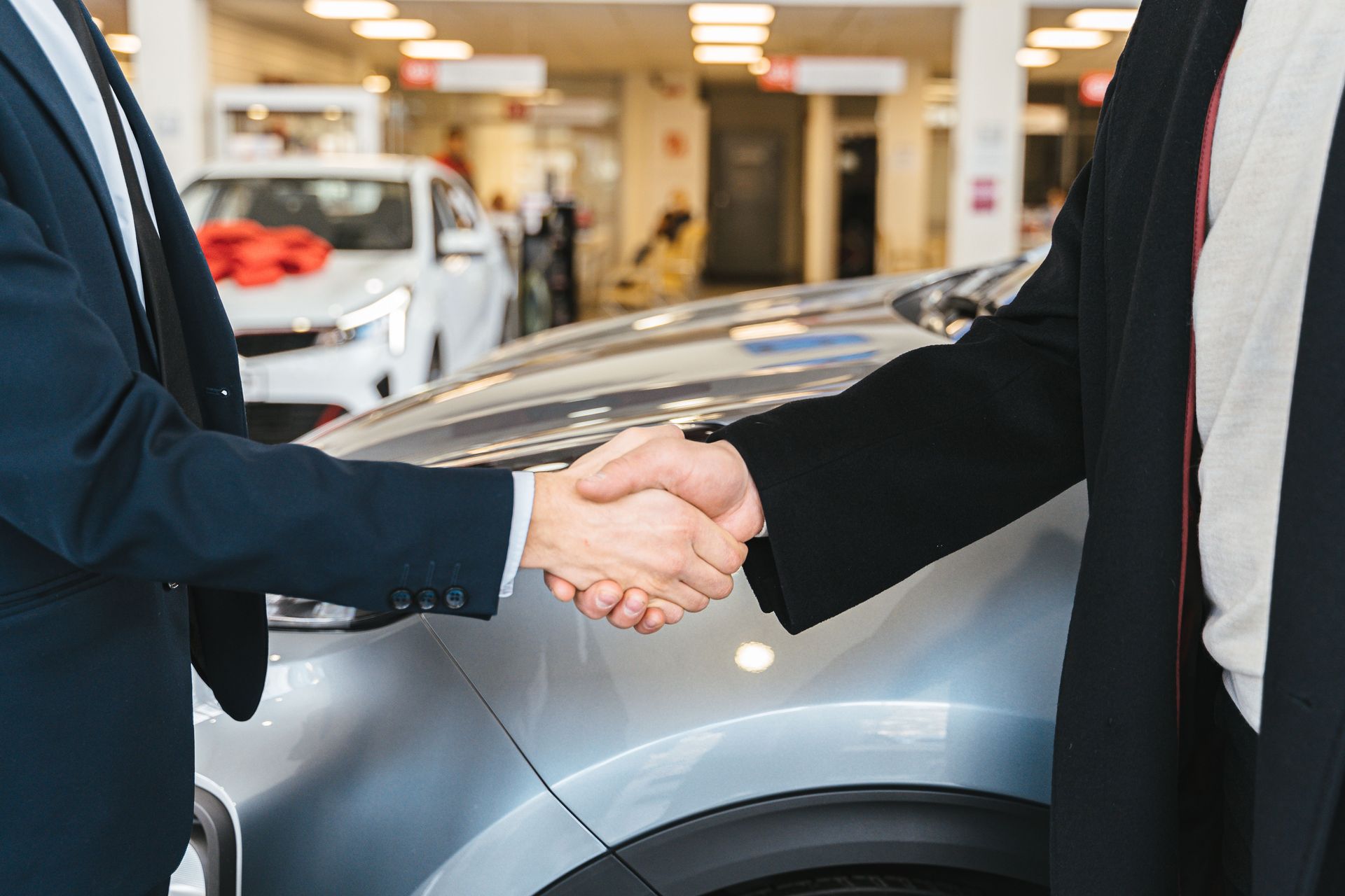 Deux personnes se serrent la main à côté d’une voiture argentée dans un showroom
