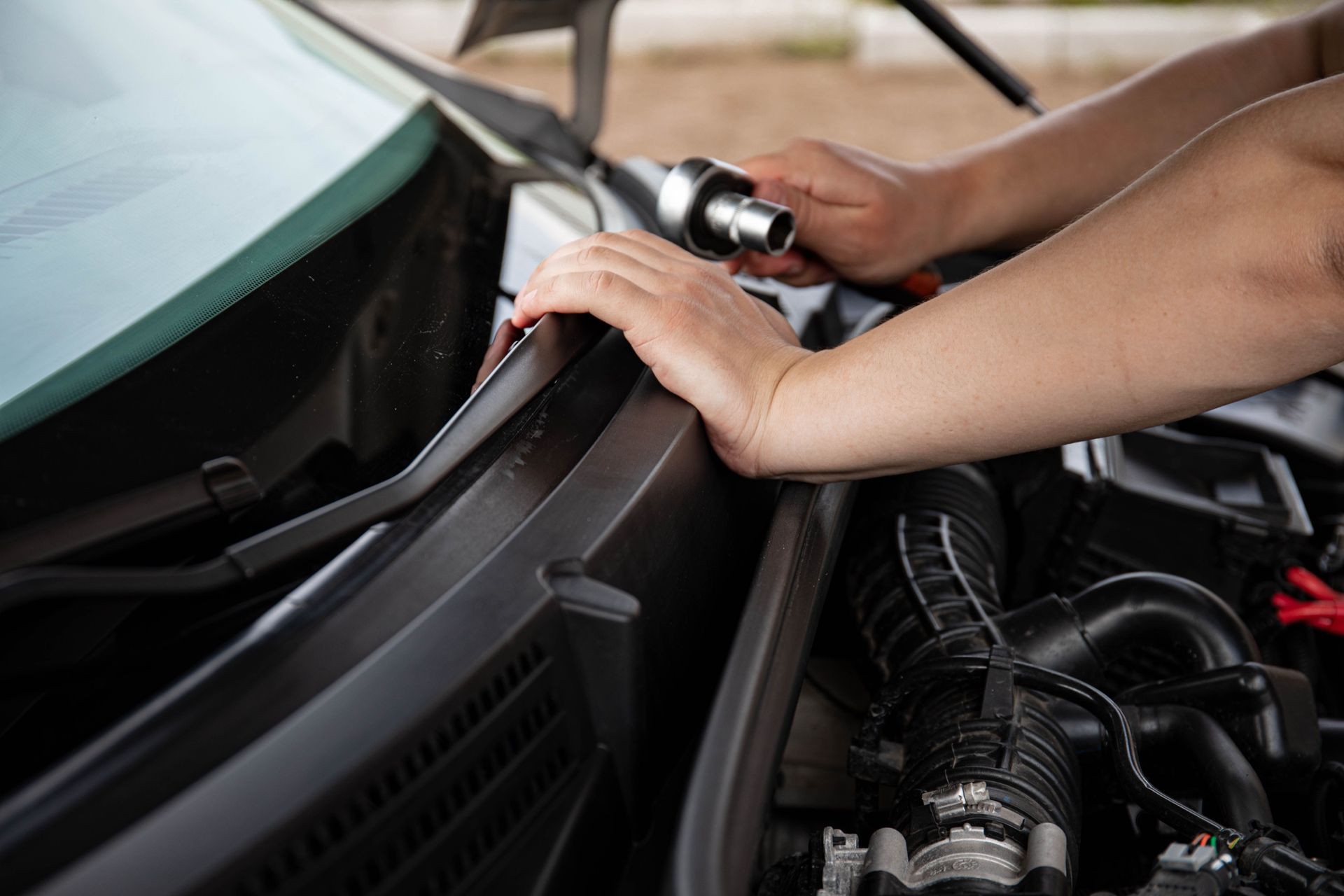 Des mains travaillant sous le capot d’une voiture, au niveau des essuie-glaces