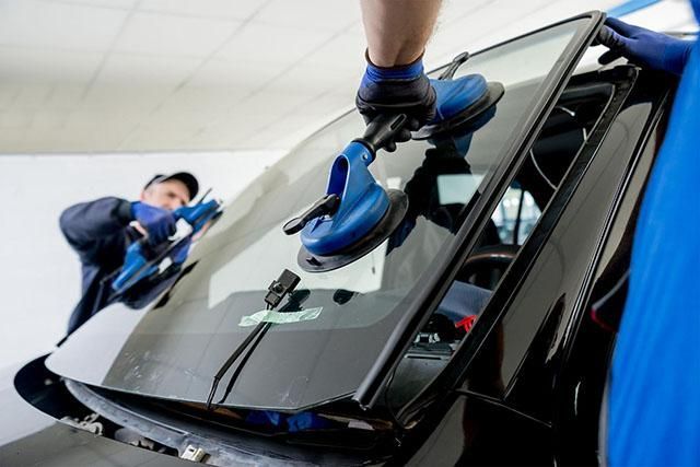 Des techniciens en uniforme bleu qui polissent le pare-brise d’une voiture noire dans un atelier