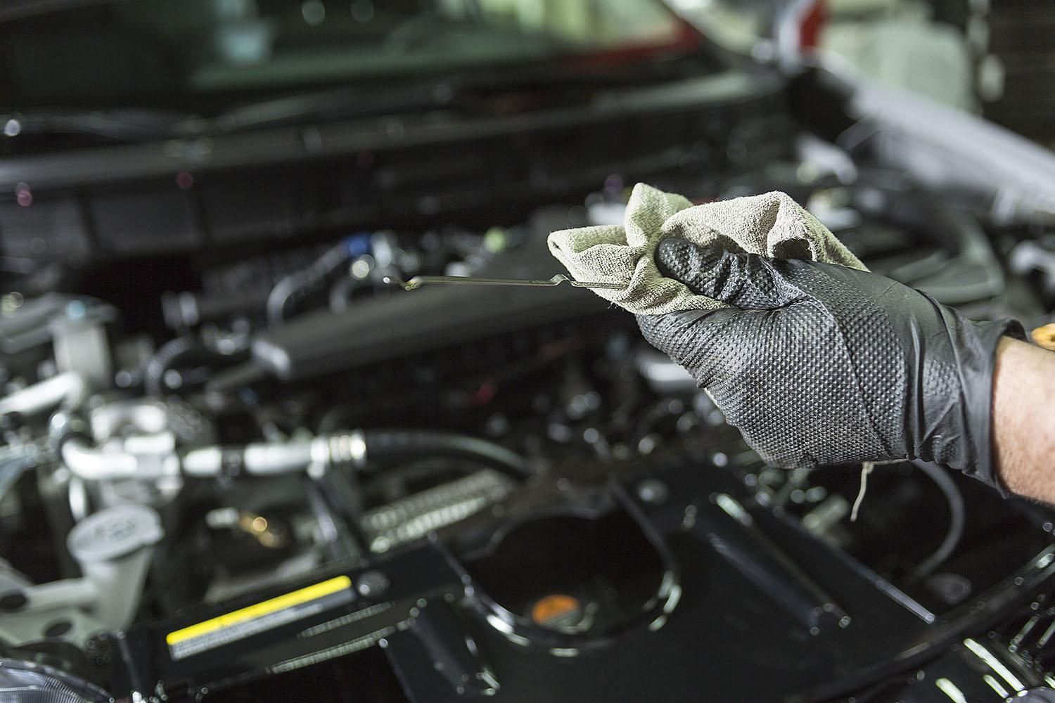 Une main gantée tenant un chiffon imbibé d’huile au-dessus du compartiment moteur ouvert d’une voiture