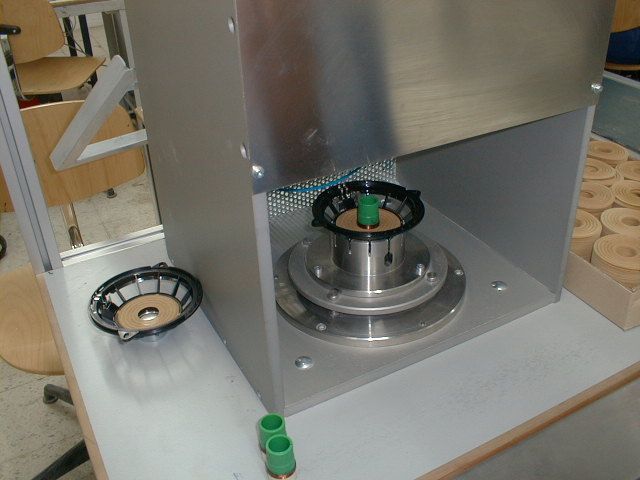 Metallmaschine mit einem zentralen Drehteil und daneben liegenden grünen und schwarzen Teilen auf einem Werkstattboden