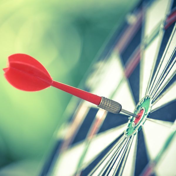 Ein roter Dartpfeil trifft eine Dartscheibe, Nahaufnahme mit verschwommenem grünen Hintergrund