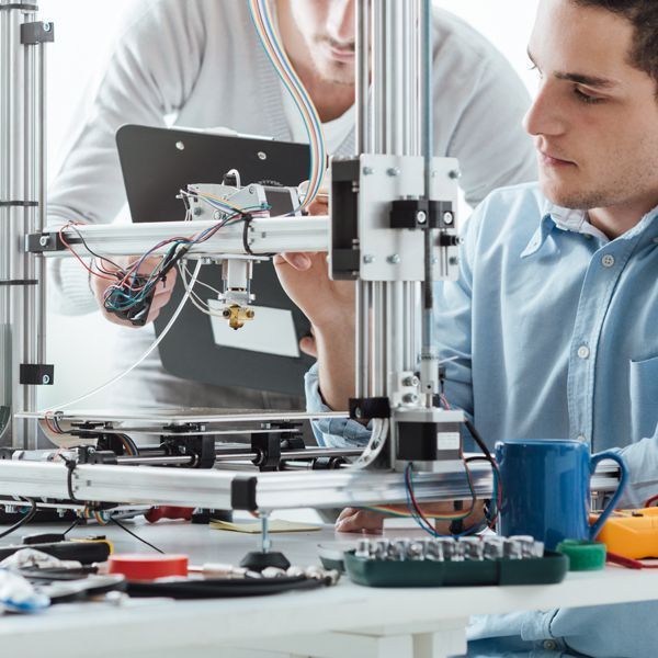 Zwei Personen arbeiten auf einem Labortisch mit Werkzeugen und Leiterplatten an einem 3D-Drucker-Prototyp.