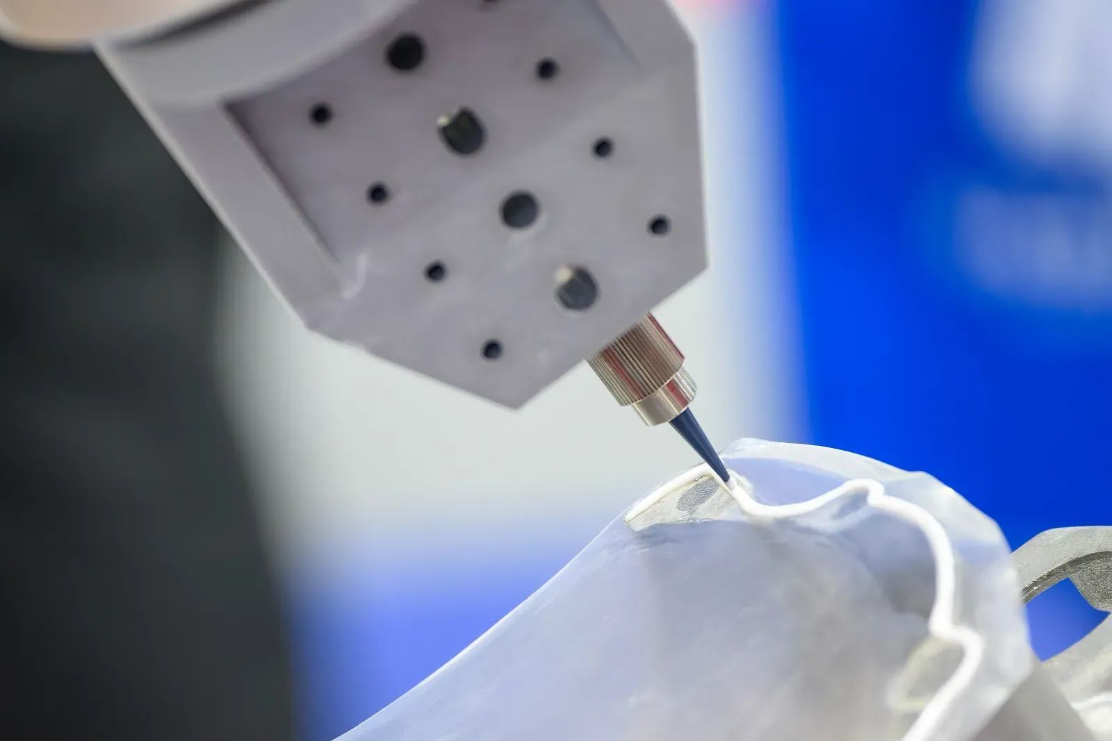 Ein Roboterarm führt in einer Fabrikumgebung eine präzise Aufgabe an einem weißen Stoff aus.